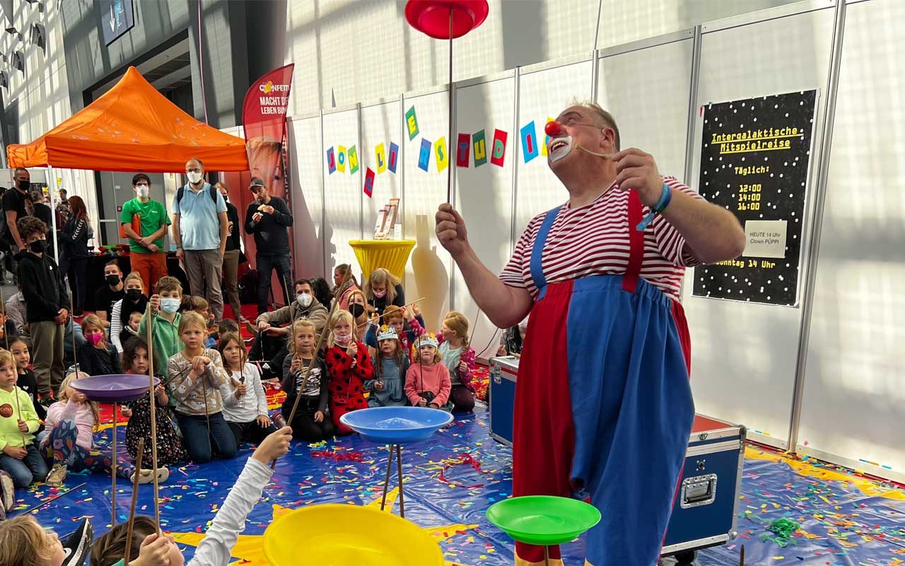 Clown Püppi begeistert Kinder beim Jonglierstudio auf der SPIEL Essen mit bunten Tellern und viel Lachen