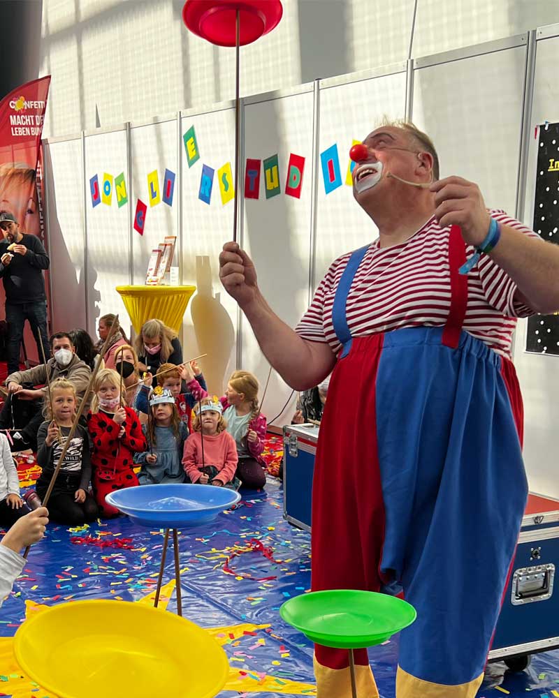 Clown Püppi begeistert Kinder beim Jonglierstudio auf der SPIEL Essen mit bunten Tellern und viel Lachen